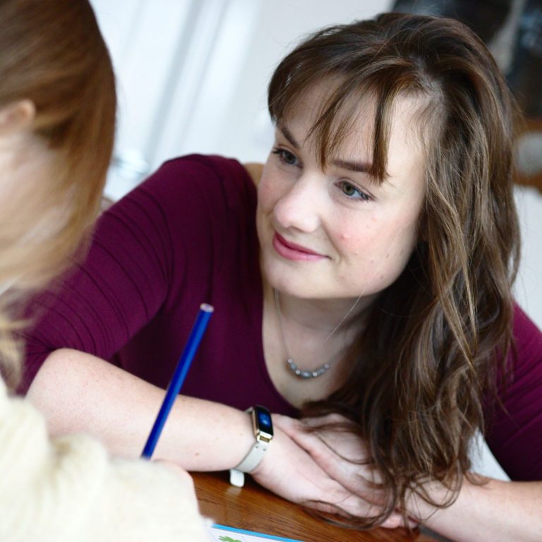 Emily Fox is smiling at her pupil, who is writing